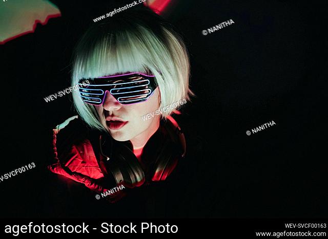 Woman with white short hair wearing neon glasses against black background