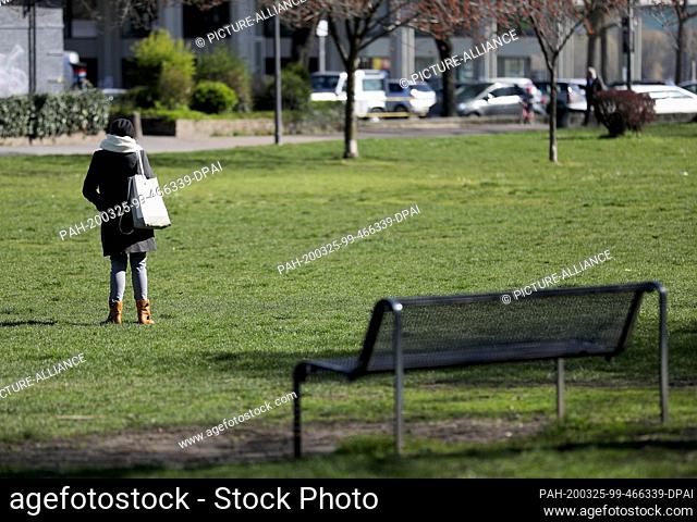 25 March 2020, North Rhine-Westphalia, Cologne: A woman stands alone in a meadow in the sun. In order to contain the coronavirus