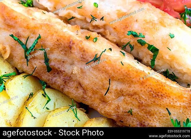 On the table on a plate two slices of fried fish, fried potatoes , dill, parsley. Presented in close-up