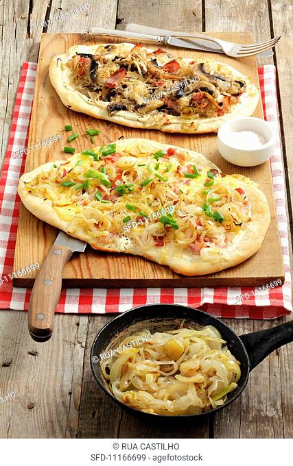 Two tarte flambées (one with sauerkraut, mushrooms and bacon and one with onions, cheese and bacon)