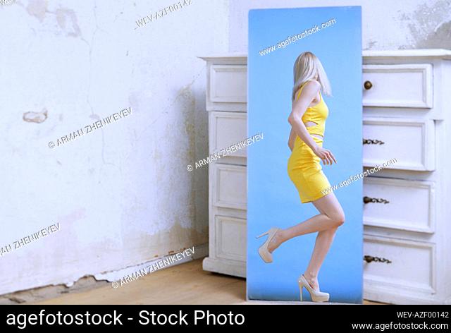 Young woman seen in mirror reflection against white wooden drawer
