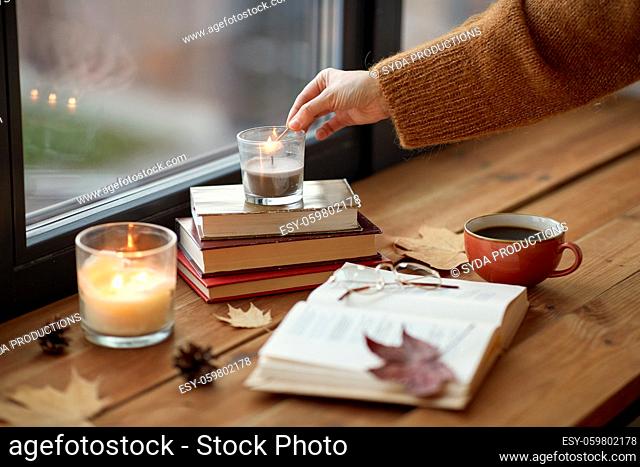hand with match lighting candle on window sill