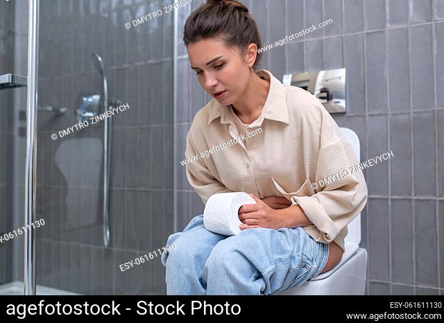 Indigestion. Young woman sitting on a toilet and suffering from indigestion