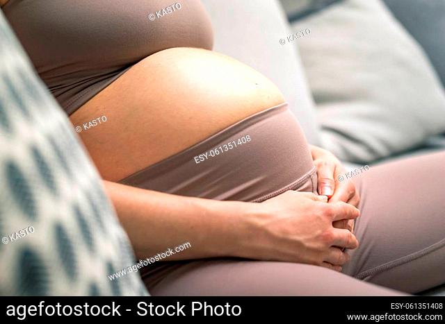 Pregnant woman belly. Pregnancy Concept. Pregnant tummy close up. Detail of pregnant woman relaxing on comfortable sofa at home