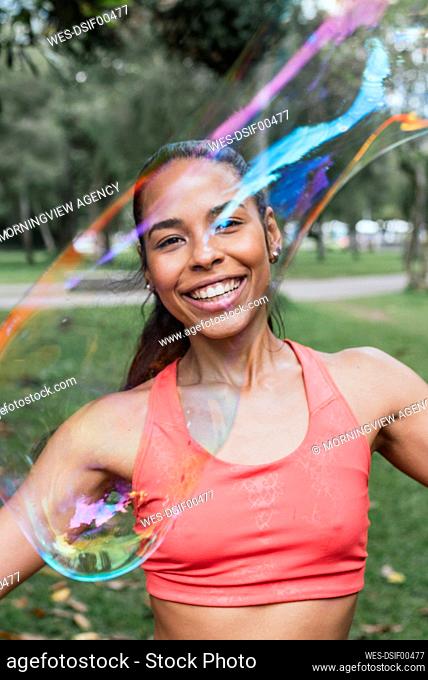 Happy female athlete seen through soap bubble at public park