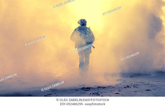 Special operations forces soldier, army ranger or commando in camo uniform, helmet and ballistic glasses walking at battlefield covered with smoke