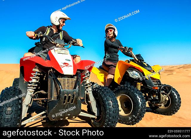 Happy couple of quad bikers laughing joyful, cheerful and fresh. Young active caucasian couple in outdoor activity driving quad ATV in Namib desert, Namibia