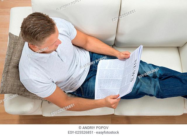 Young Man Sitting On White Sofa Reading Newspaper