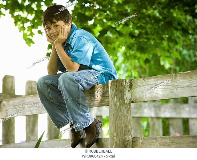 Portrait of a boy sitting on a wooden fence