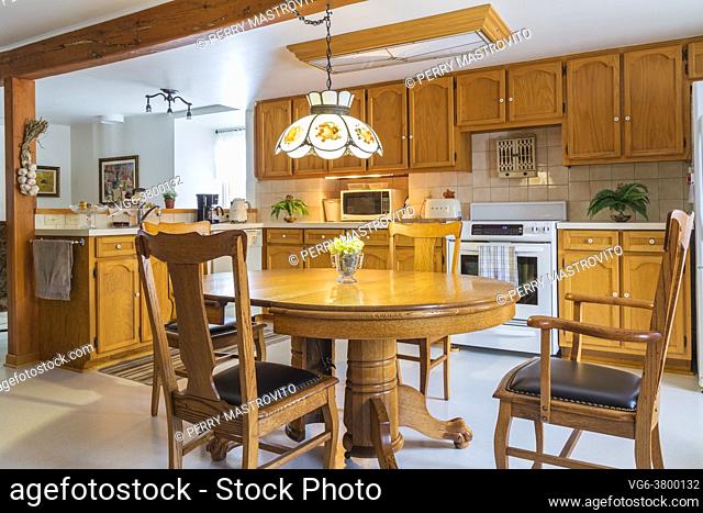 Red pine wood claw foot dining table with red oak wood and black leather seat high back chairs in kitchen with oak wood cabinets and white ivory linoleum...