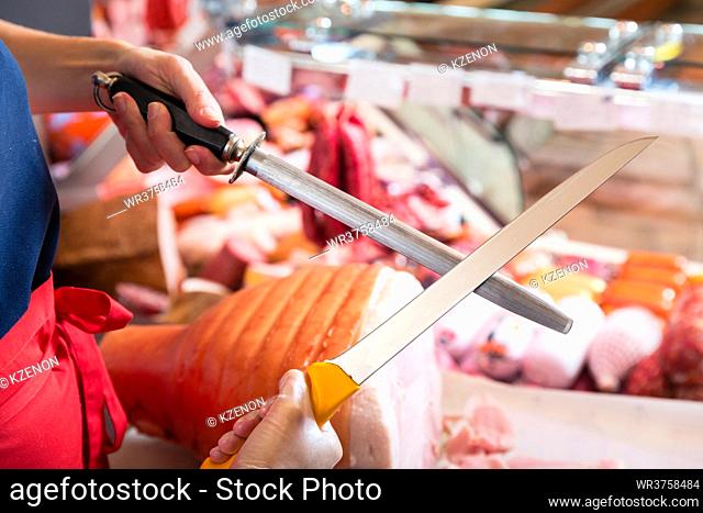 Butcher woman sharpening her knifes to cut ham