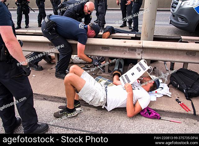13 August 2022, Hamburg: Police officers try to detach two climate activists connected with an iron pipe during a blockade on the Köhlbrand Bridge