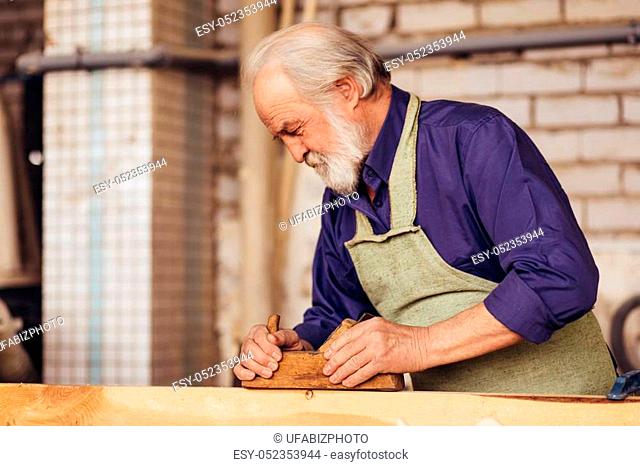 close-up side view image of senior citizen smoothing wooden board for furniture