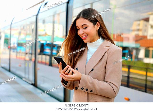 Happy beautiful woman holding cellular updating information about city transport on web page. Smiling business woman satisfied with online ticket service paying...