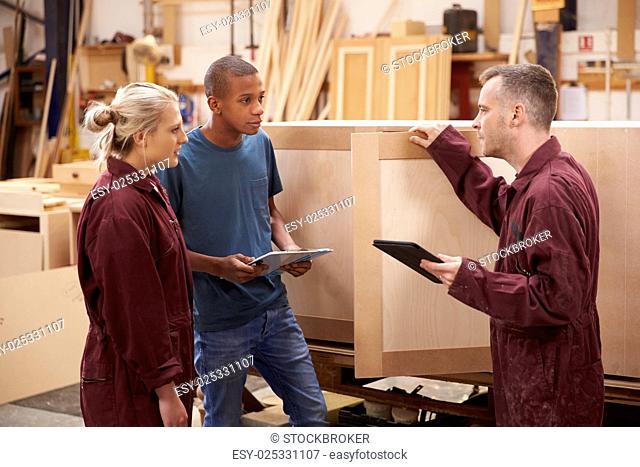 Carpenter With Apprentices Building Furniture In Workshop