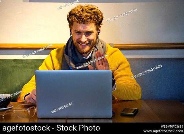 Smiling businessman gesturing during video call on laptop at cafe