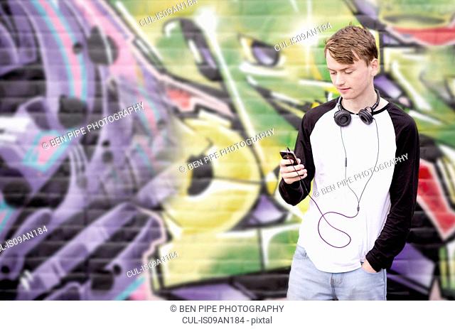Teenager with mp3 player standing against wall with graffiti