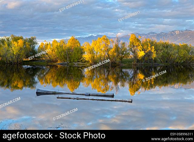 A late afternoon photo of the clouds and trees reflecting off the calm pond behind the Ninpipes Lodge north of St. Ignatius, Montana