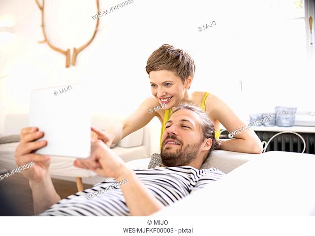 Happy young couple with tablet in living room at home