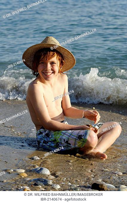 Boy sitting on a beach in the water and looking happy