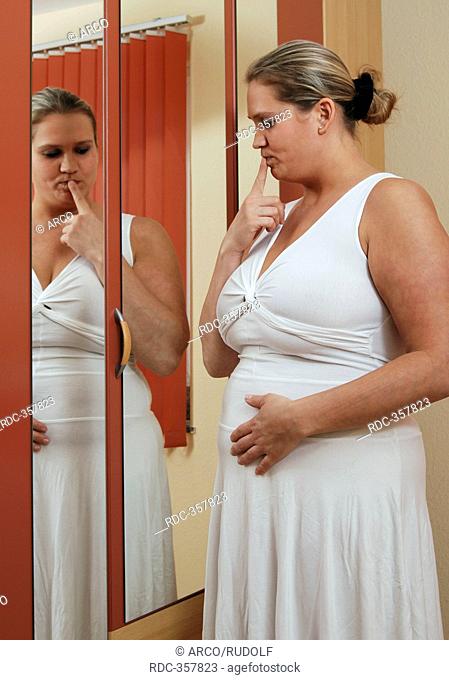 Chubby woman with big belly in front of mirror, looking at her physique