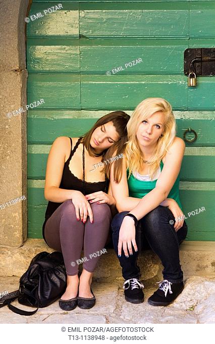 Two girlfriends are sitting tired on the porch after a night out