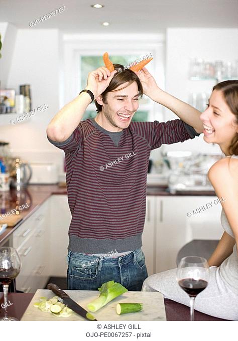 Man making horns with carrots in kitchen