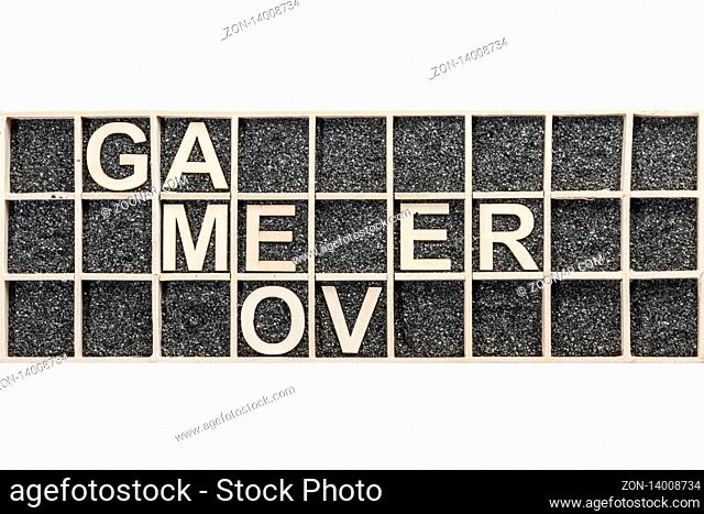 Plywood letters arranged in a collecting box with black decorative sand representing the word GAME OVER in top view on white background