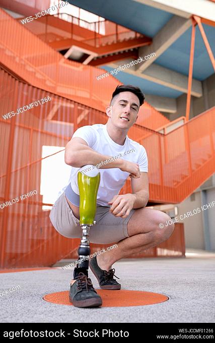 Handsome young amputated man crouching against orange staircase