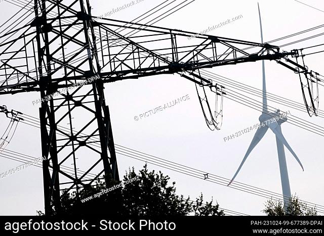 PRODUCTION - 23 October 2023, Lower Saxony, Winkelsett: A wind turbine stands behind a high-voltage power line in a field