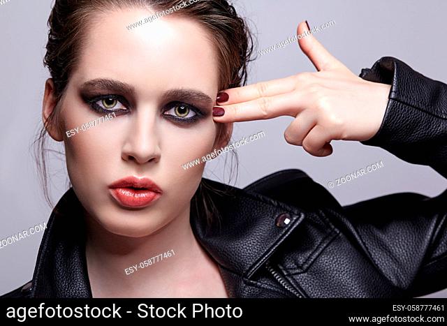 Portrait of female in black leather jacket and fingers at the temple. Woman with unusual beauty evening makeup. Girl with perfect skin