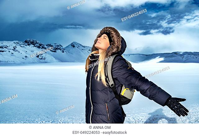 Beautiful woman with raised hands enjoying sun light in cold frosty day in the valley among high mountains, happy winter vacation, Iceland