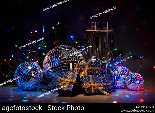 Champagne flutes, mirror balls (disco ball), fir branch, on dark background with colorful LED lights garland. New Year and Christmas