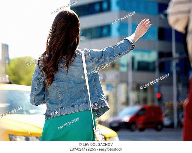 gesture, transportation, travel, tourism and people concept - young woman or teenage girl catching taxi on city street or hitch-hiking