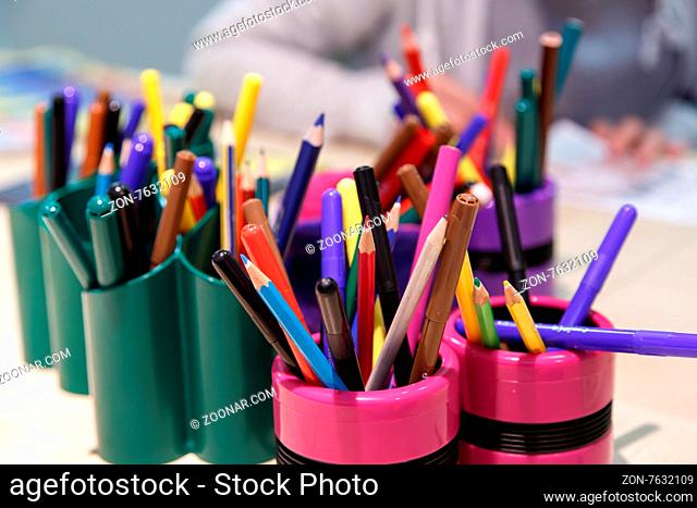 Close up detailed view of heap of multicolored dry paint pencils in pencilcases, with a painting child background