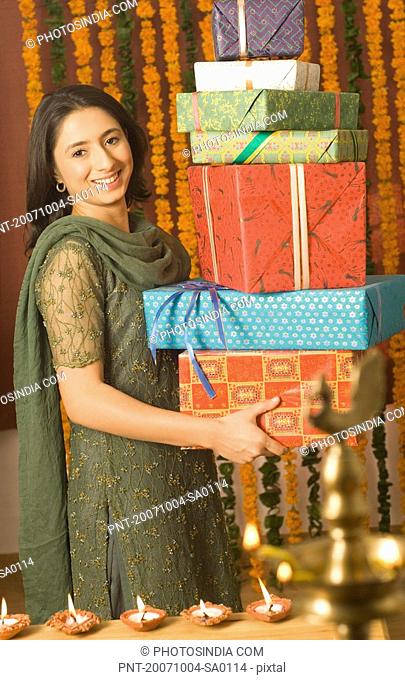 Portrait of a young woman holding a stack of diwali gifts and smiling