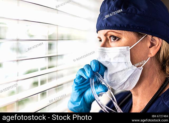Female doctor or nurse on break at window wearing medical face mask and goggles