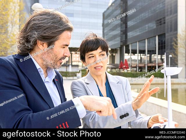 Male and female engineers discussing over wind turbine model in office park