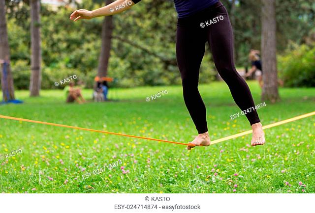 Lady practising slack line in the city park. Slacklining is a practice in balance that typically uses nylon or polyester webbing tensioned between two anchor...
