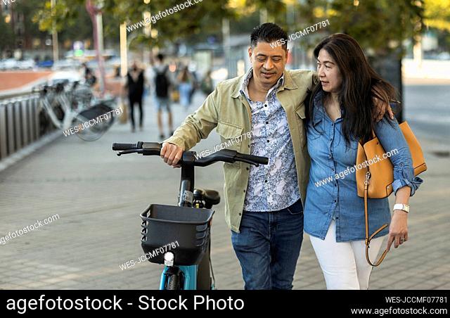 Mature couple walking with electric bicycle on footpath