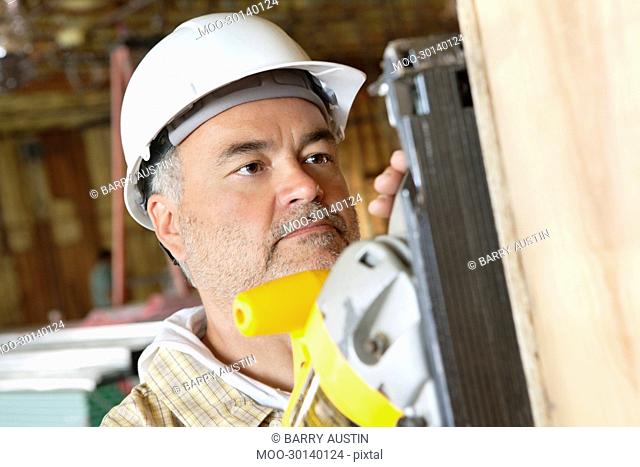 Serious male construction worker cutting wood with a power saw
