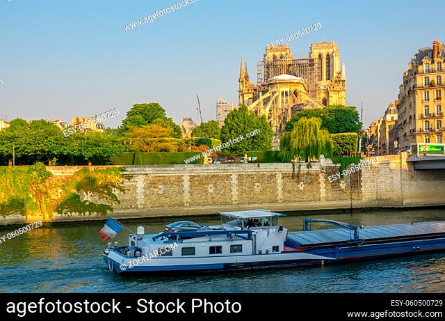France. Paris. Sunny summer morning on the Seine embankment. View of Notre Dame in scaffolding after a fire in 2019. Barge on the river