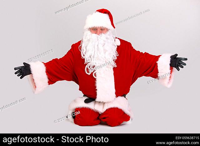Full size portrait of Santa kneeling on ground outspreading arms, looking down, isolated on gray background