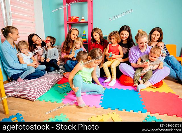 Group of kids sitting on a floor surrounded by mothers with their kids. Adaptation time at the kindergarten or daycare
