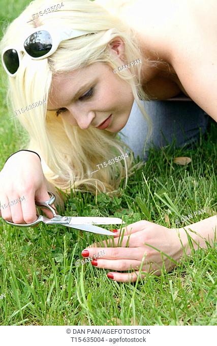 Young woman cutting grass like a hair dresser cutting hair using a pair of scissors, funny, humor