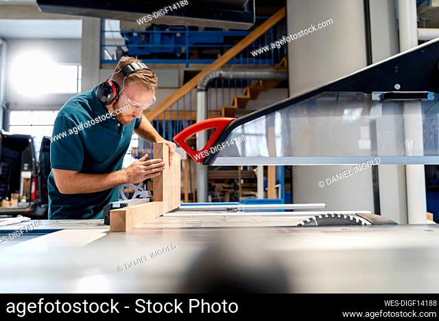 Carpenter cutting plank on circular saw in production hall