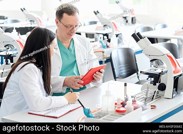 Scientists in white coats using tablet in lab
