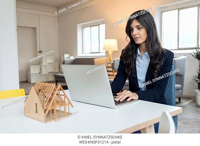 Young businesswoman using laptop on table next to architectural model