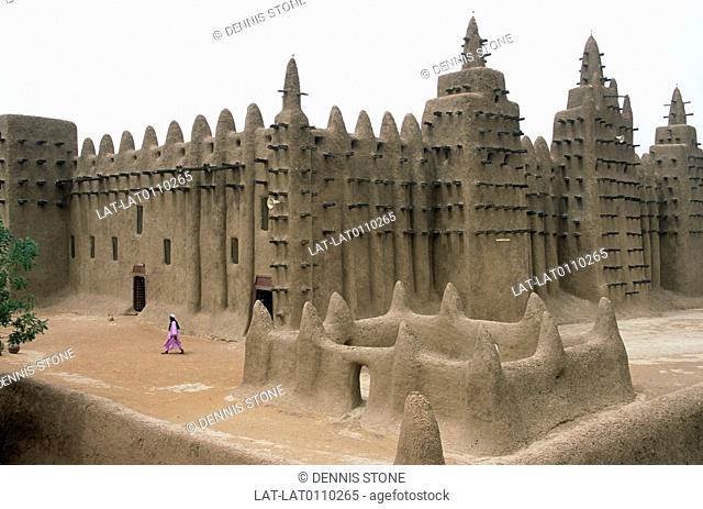 City built of mud. Mosque. Rounded wall shapes. Iron spikes on walls. Man in pink robe walking in courtyard