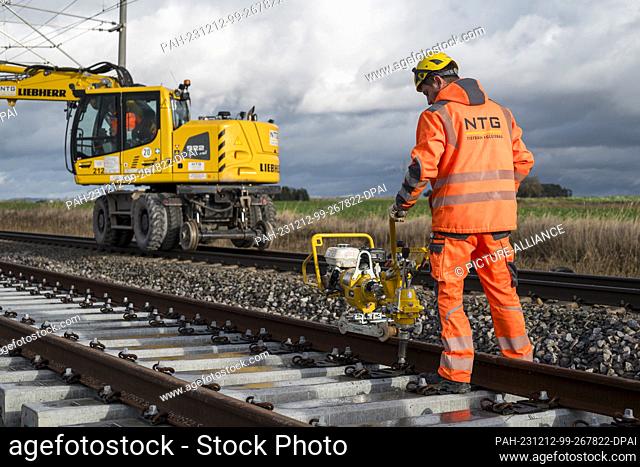 PRODUCTION - 11 December 2023, Bavaria, Eltersdorf: A worker bolts the track to the concrete sleepers at the railroad construction site for the ICE line between...